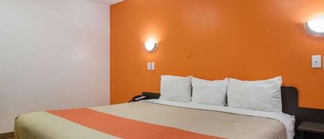 Una habitación de hotel con una cama, una mesita de noche, un teléfono y una lámpara fijada a la pared.