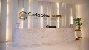 Ein Empfangsschalter mit Marmorplatte, ein Logo mit kreisförmigem Wappen und die Aufschrift 'Cartagena BEACH Exclusive Resort Residences' an der Wand dahinter.