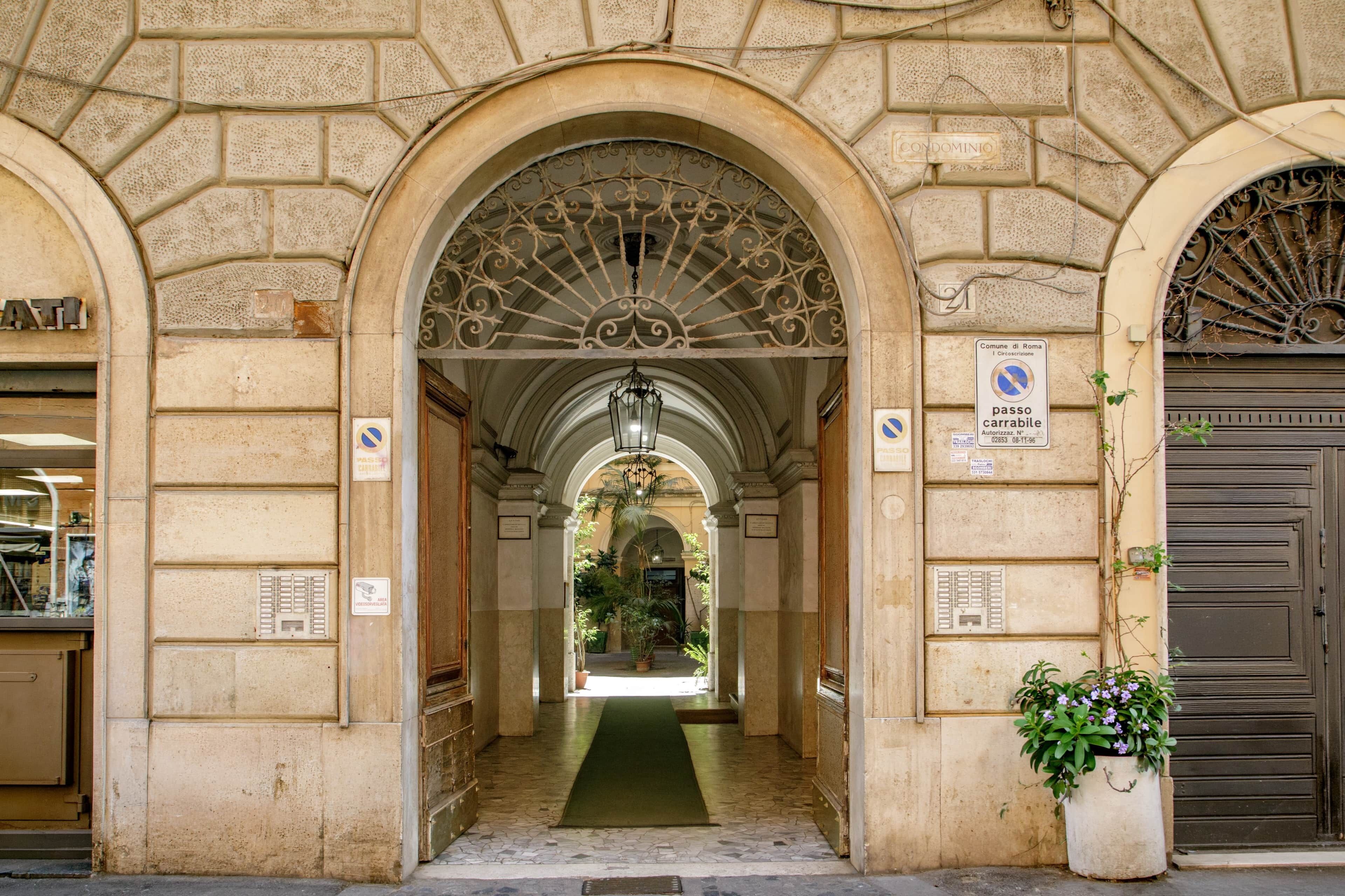 A stone building with an arched entrance, a green carpet, and a potted plant.