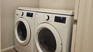 Un cuarto de lavandería con dos lavadoras de carga frontal y un estante metálico encima.