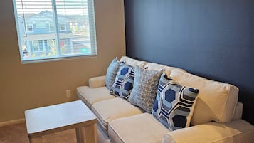Un salon avec un canapé beige, une table basse en bois et une fenêtre avec des stores.