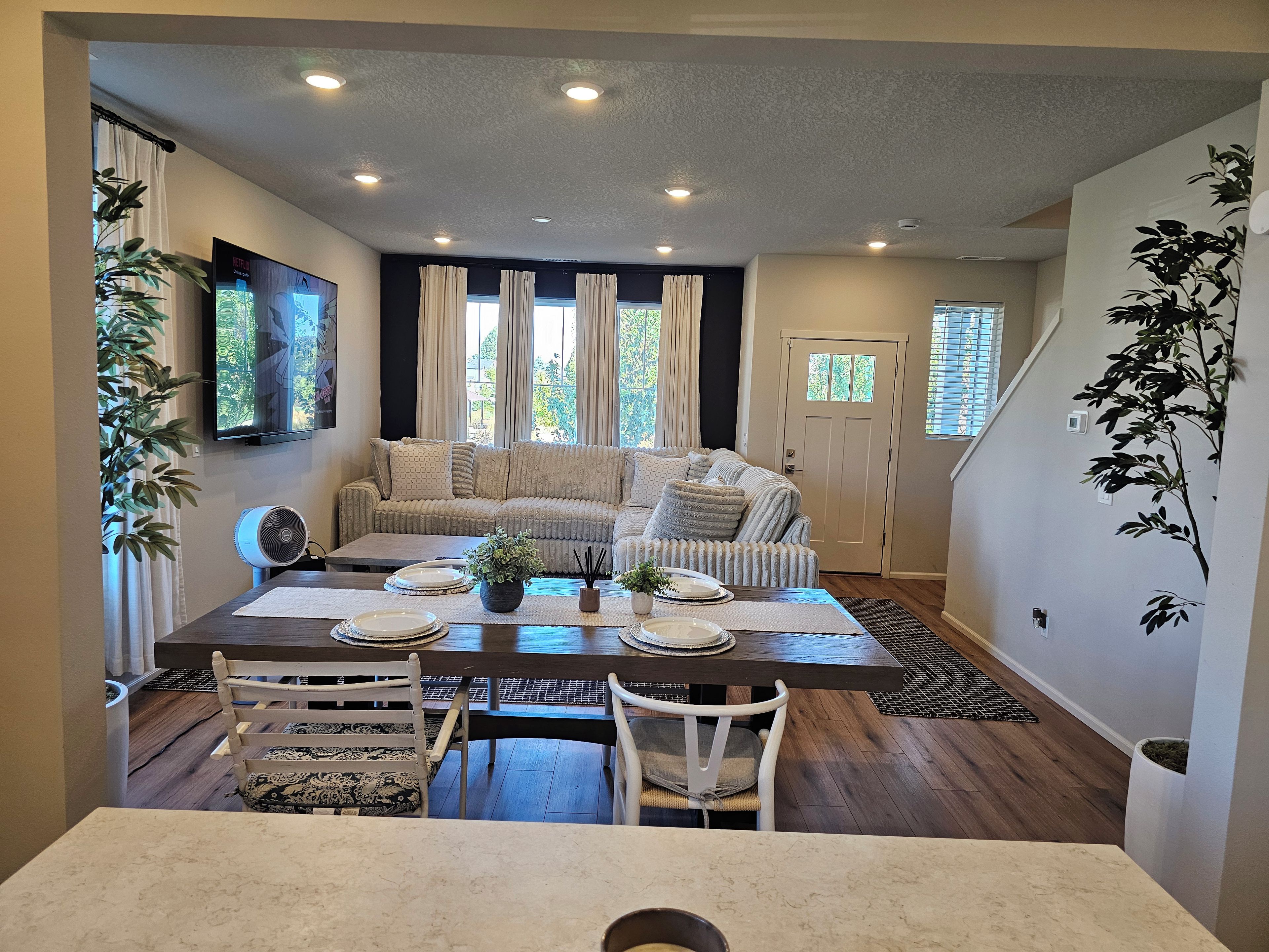 A dining area with a table set for four, a sofa in the background, and a television mounted on the wall.
