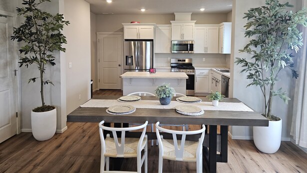 Una cocina moderna con armarios blancos, electrodomésticos de acero inoxidable y una mesa de comedor de madera con sillas.