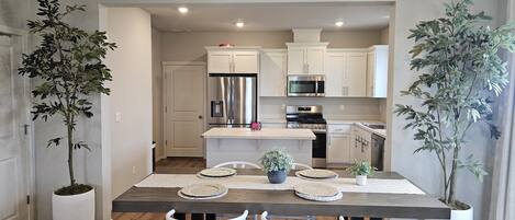 A modern kitchen with white cabinets, stainless steel appliances, and a wooden dining table with chairs.