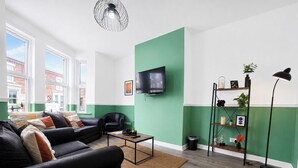Ein modernes Wohnzimmer mit einer schwarzen Couch, einem Couchtisch, einem an der Wand befestigten Fernseher und einer Stehlampe.