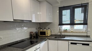 Een moderne keuken met witte kasten, een granieten aanrechtblad, een inbouwoven, een magnetron en een vaatwasser.