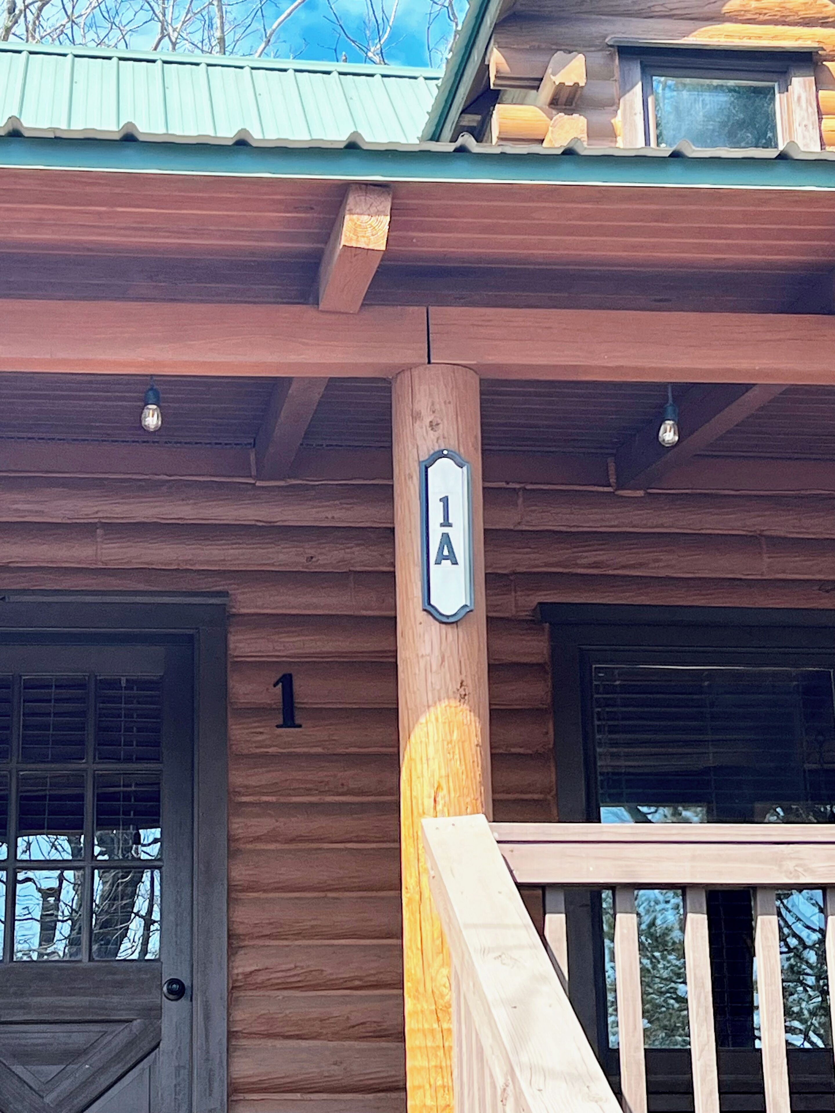 Eine Holzhütte mit der Nummer 1, einer Veranda und einem Fenster mit Blick auf Bäume.
