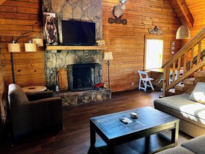 A cozy cabin interior with a stone fireplace, wooden walls, a television, and a staircase. - The Roosevelt - Close to Mountainside pool! (Warm Springs)