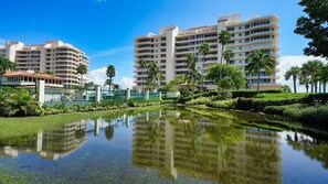 A hotel with multiple floors, a central courtyard with a reflecting pool, and palm trees. - Luxury Rental in Bay Isles facing the Bay (Longboat Key)