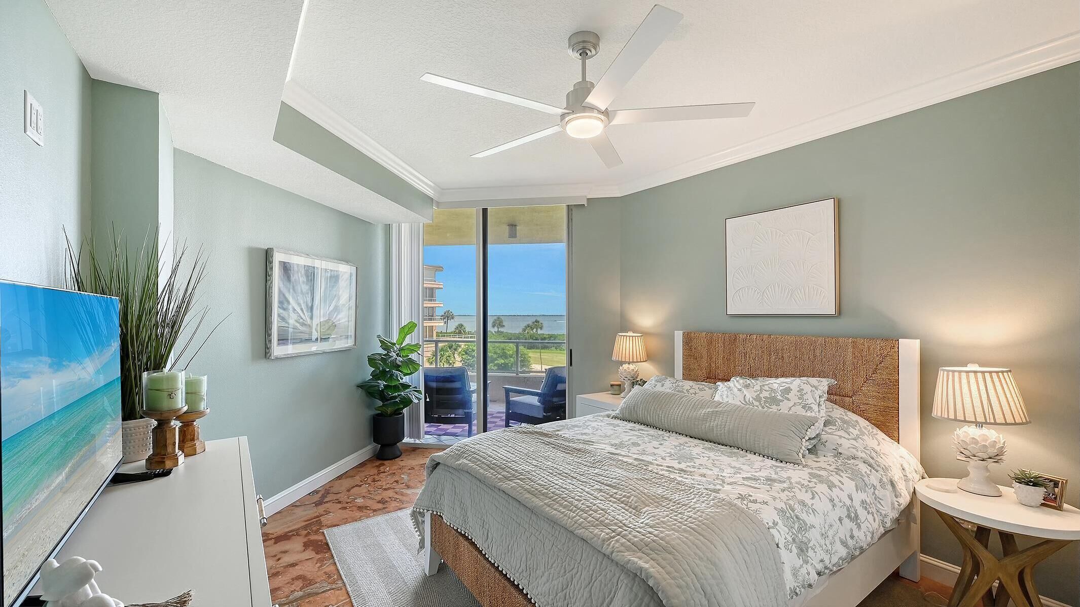 Bedroom with woven headboard, floral bedding, ceiling fan, and sliding glass doors opening to balcony.