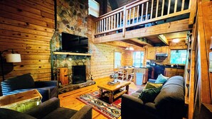 Ein Interieur einer Hütte mit Kamin aus Stein, Holzmöbeln, einem Balkon und einer Küchenzeile.