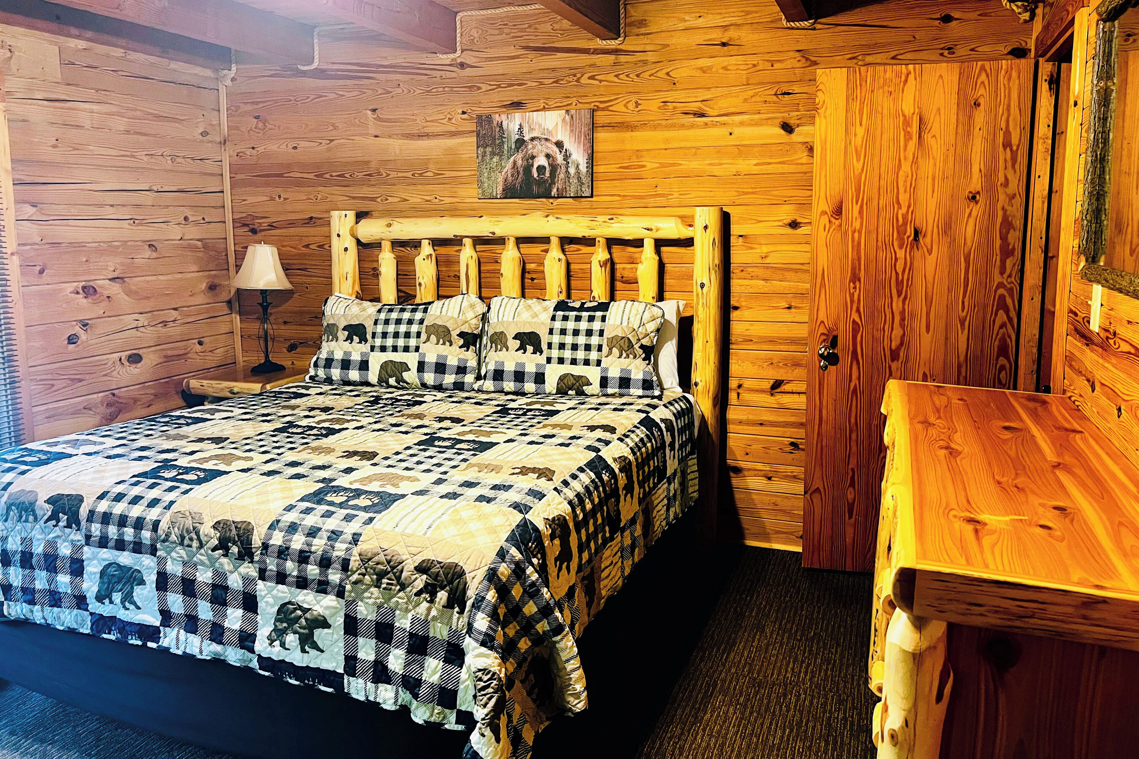 A wooden cabin-style room with a bed, a nightstand, a lamp, and a wooden table.