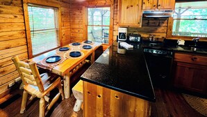 Ein Holzblockhaus-Interieur mit Esstisch, Stühlen, einer Kaffeemaschine, einem Toaster und einem Herd.