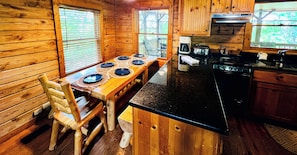 A wooden cabin interior with a dining table, chairs, a coffee maker, a toaster, and a stove.