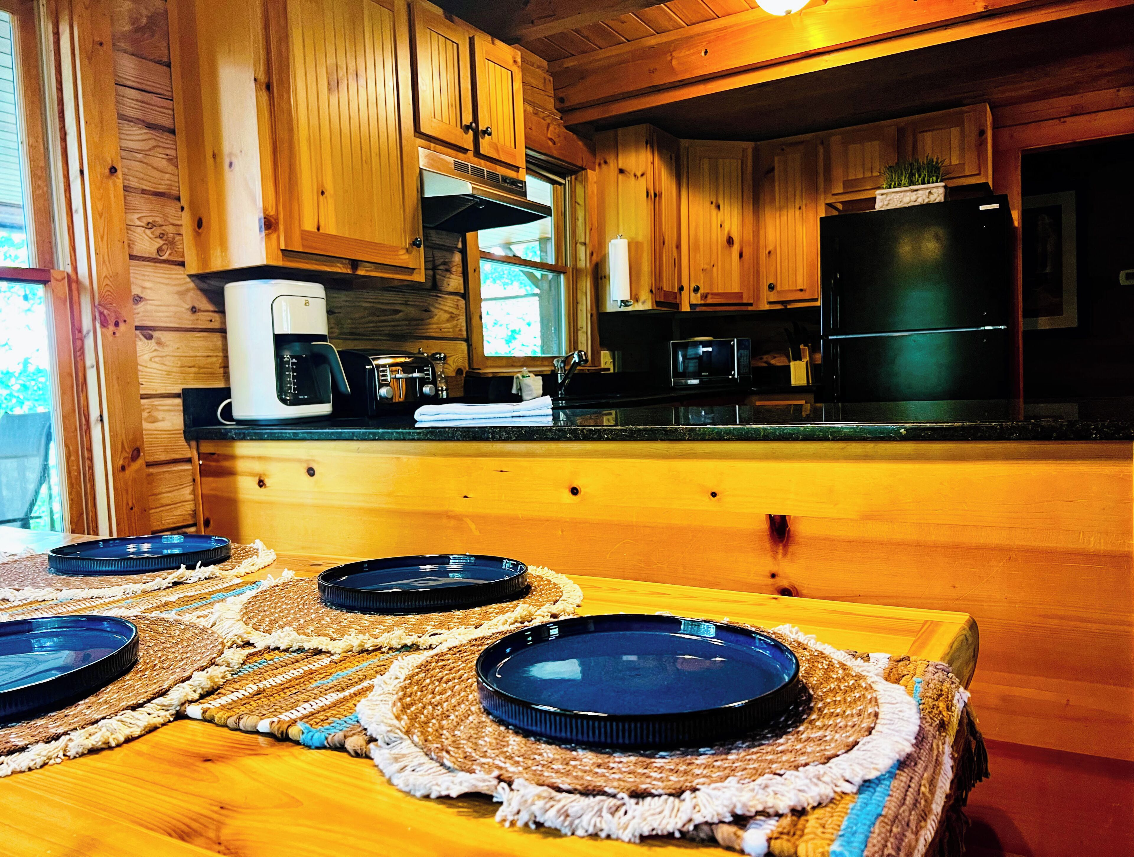 Interior de una cabaña de madera con cocina que incluye armarios de madera, microondas, tostadora y refrigerador.