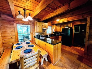 A wooden cabin interior with a kitchen, dining table, and a view through a window. - Perfect cabin for large families (Warm Springs)