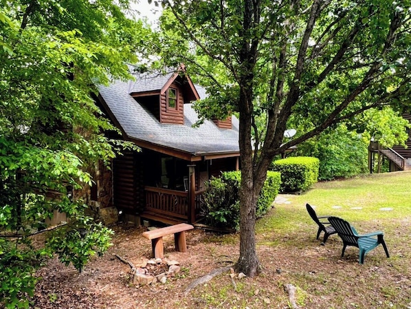 A cabin with a porch, a bench, and a tree in the foreground.