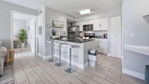 A modern kitchen with white cabinets, a stainless steel refrigerator, and a microwave. There are three bar stools and a trash can. - Lakeside view retreat at Villas del Sol (Kissimmee)