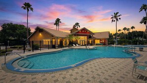 A swimming pool with a tiled deck, palm trees, and a building with a red roof. - Lakeside view retreat at Villas del Sol (Kissimmee)