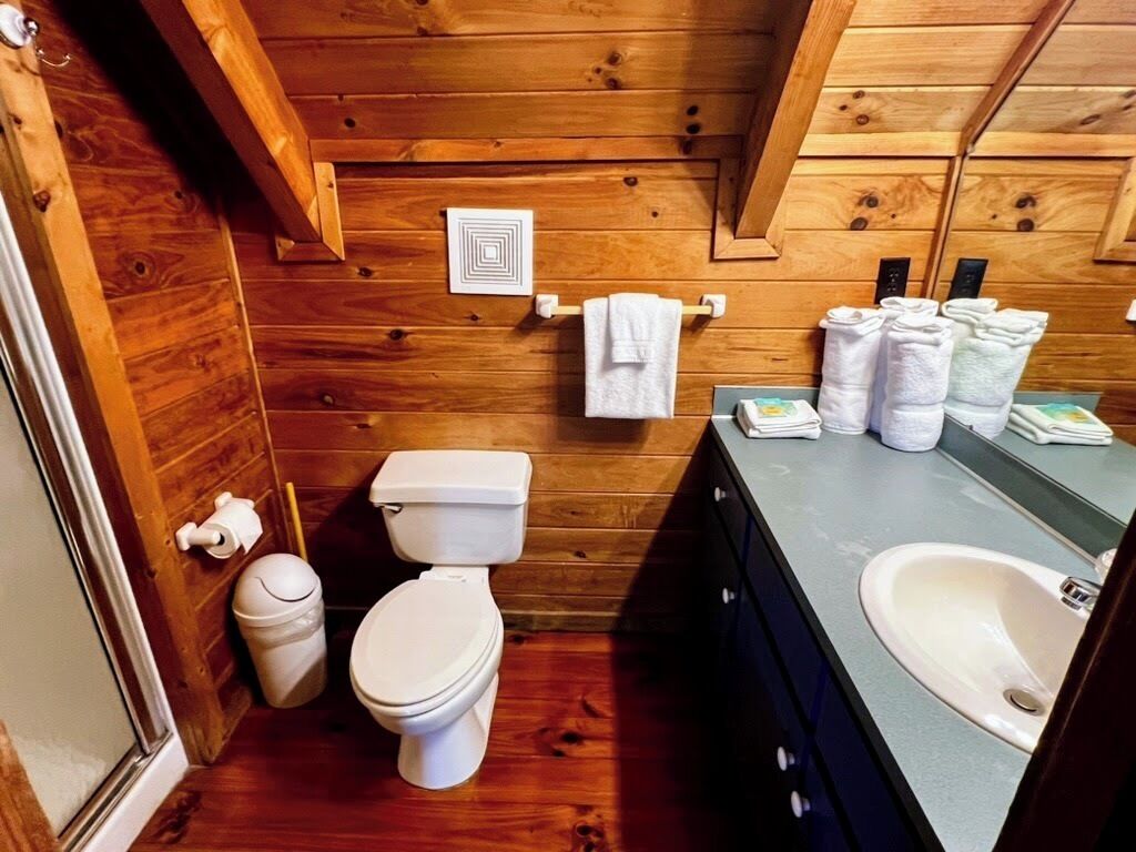 A wooden-paneled bathroom with a toilet, sink, and towel rack.