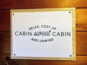 A sign with the text 'RELAX, COZY UP CABIN sweet CABIN AND UNWIND' mounted on a wooden surface. - Beautiful sunsets, decks, firepit! (Warm Springs)