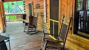 Eine Holzhütte mit Veranda, Schaukelstühlen, einem Tisch und einem Fenster.