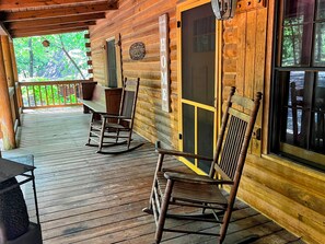 A wooden cabin with a porch, rocking chairs, a table, and a window. - Shabby Chic meets the mountains! Sleeps 6 (Warm Springs)