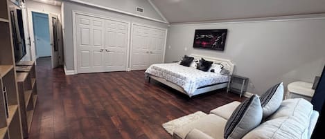 A bedroom with a bed, a couch, a white door, and a hallway leading to another room.