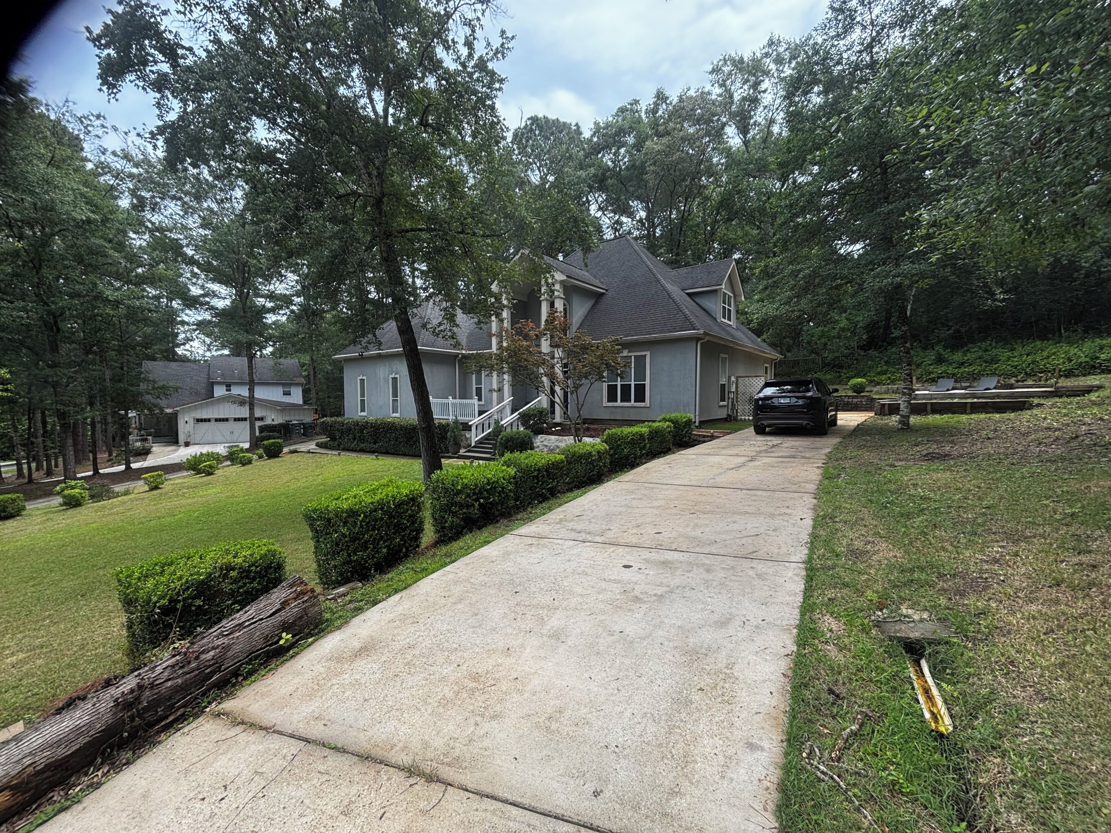 A residential driveway leading to a house with a garage, surrounded by trees and a well-maintained lawn.