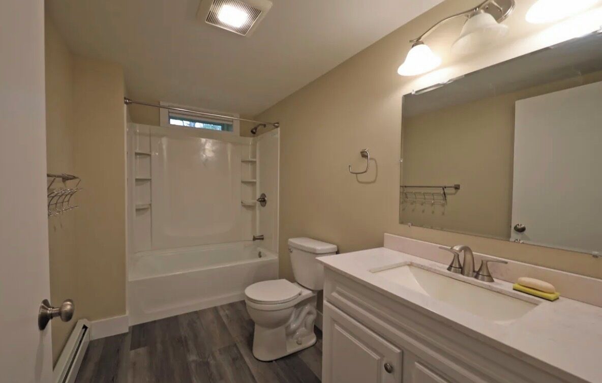 A bathroom with a bathtub, toilet, and vanity with a mirror.