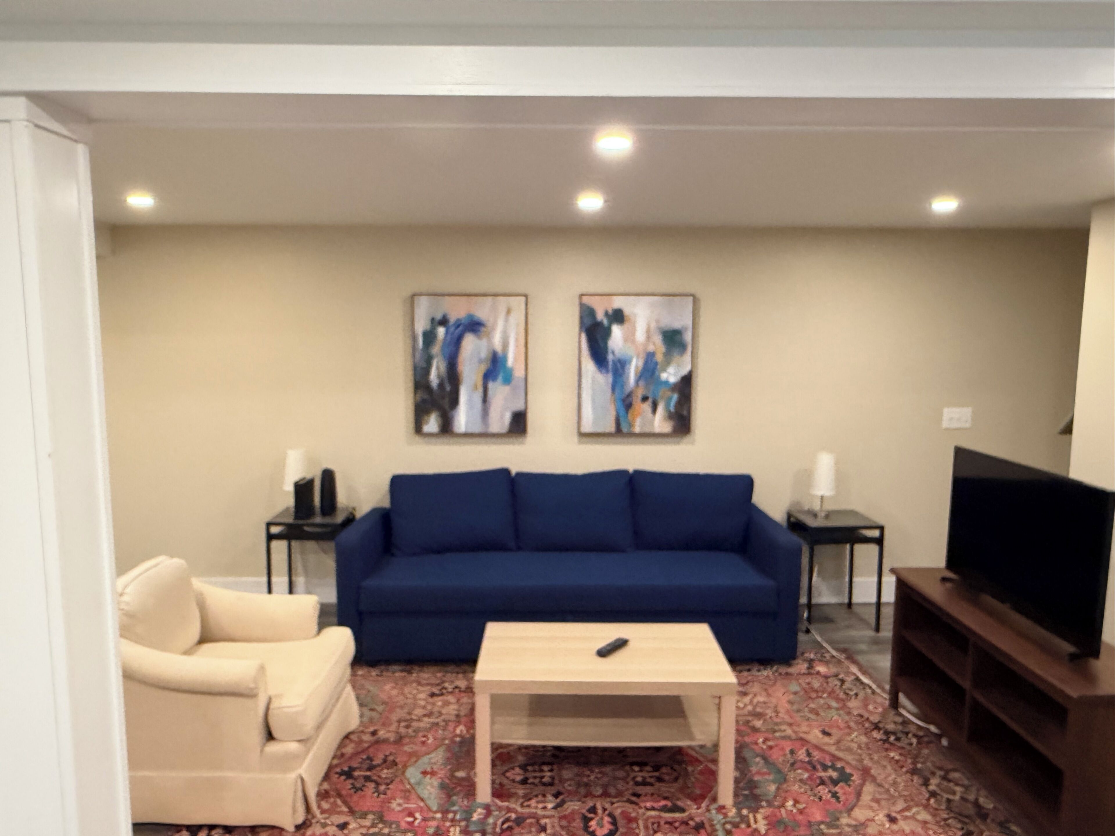 Un salon avec un canapé bleu, un fauteuil beige, une table basse, un téléviseur et deux tableaux abstraits accrochés au mur.