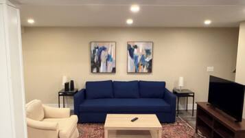 Un salon avec un canapé bleu, un fauteuil beige, une table basse, un téléviseur et deux tableaux abstraits accrochés au mur.