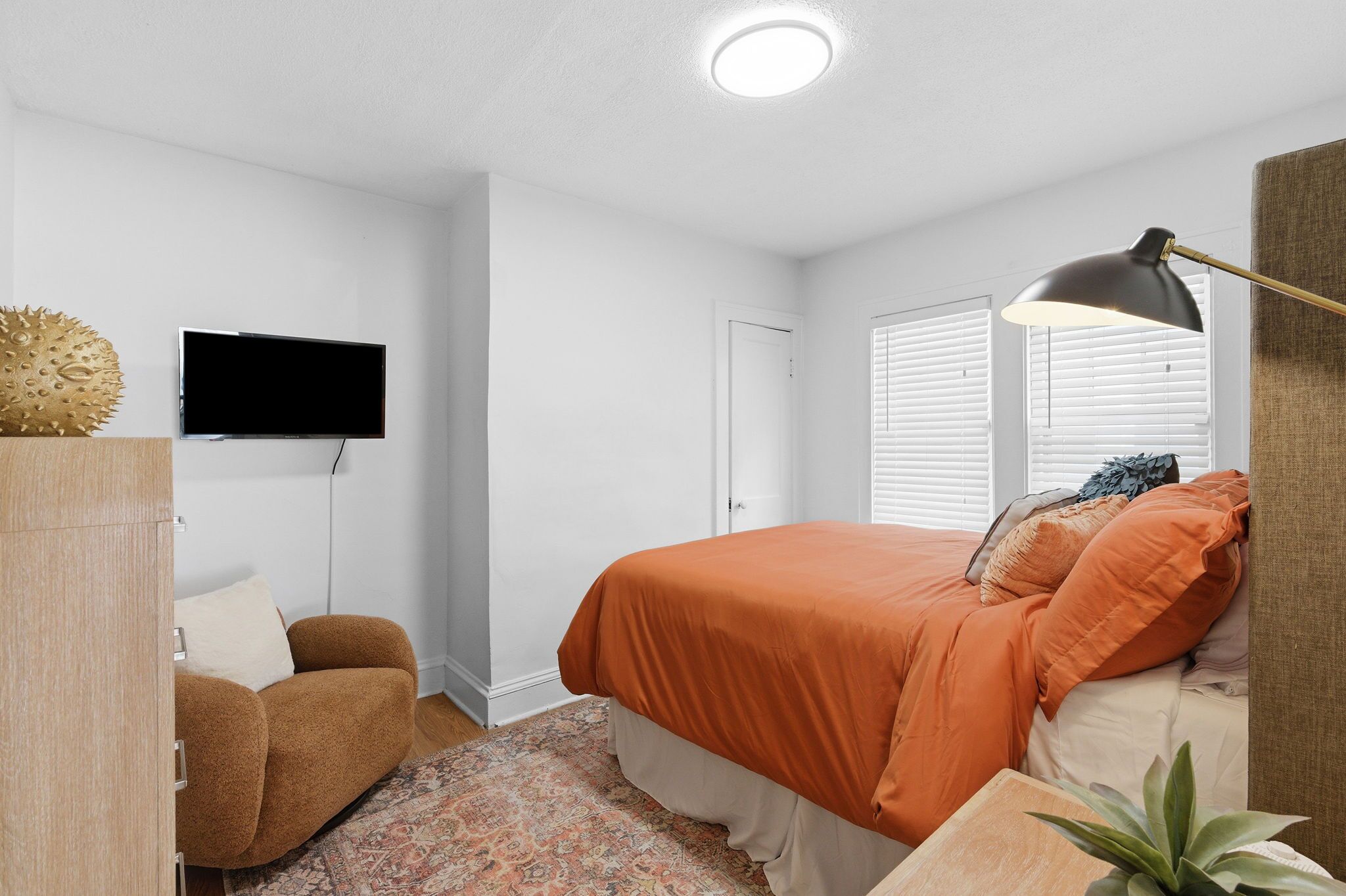A bedroom with a bed, a television, a desk, a chair, and a door.