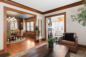 A spacious living room with a wooden floor, a dining area with a table and chairs, a fireplace, and a large window. - Charming 2BR Lake Erie Retreat Near Gordon Square (Cleveland)