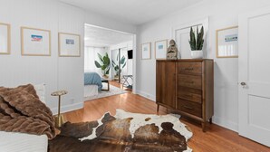 Una stanza con un letto, una cassettiera in legno, un tappeto in pelle di mucca, quadri appesi al muro e una pianta in vaso.