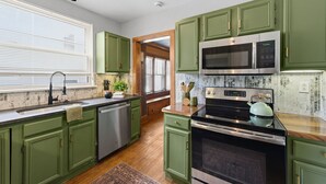 Una cucina con mobili verdi, una lavastoviglie in acciaio inossidabile, un forno a microonde e un piano cottura.
