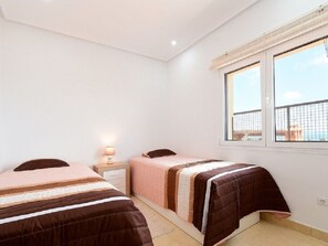 Ein Schlafzimmer mit zwei Betten, einem Nachttisch, einem Fenster und Blick ins Freie.