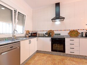 Una cocina con armarios blancos, lavavajillas, estufa y microondas.
