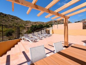 Eine Terrasse mit Holz-Pergola, Liegestühlen und einem Tisch, mit Blick auf eine hügelige Landschaft.