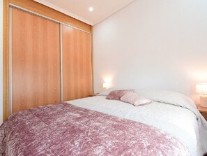 Un dormitorio con cama, un armario de madera y una mesita de noche con lámpara.