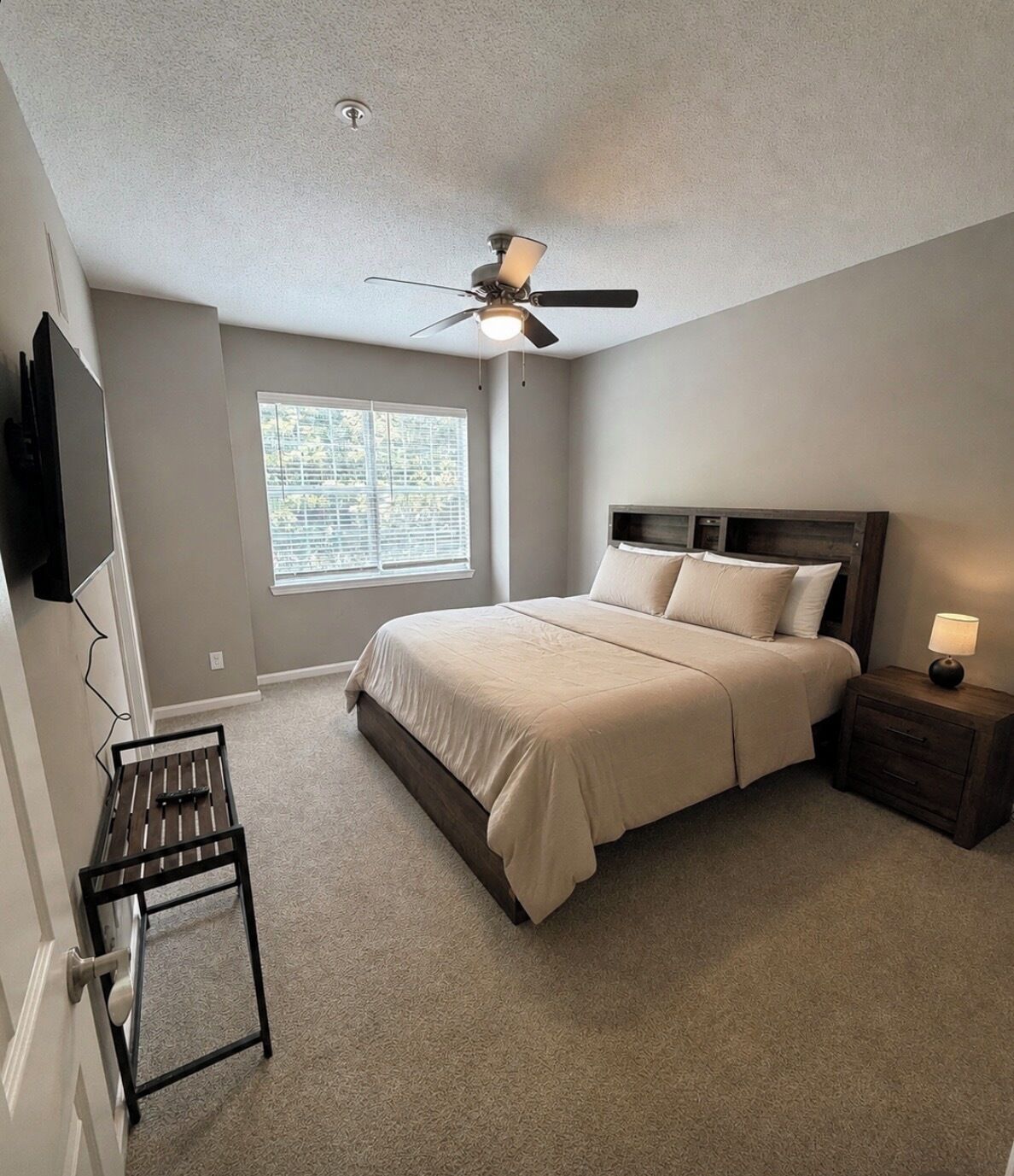 Une chambre à coucher avec un lit, un ventilateur de plafond, une fenêtre, un téléviseur et une table de chevet.
