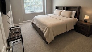 Ein Schlafzimmer mit Bett, Deckenventilator, Fenster, Fernseher und Nachttisch.