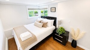Quarto com cama, mesa de cabeceira, abajur e um vaso de planta.