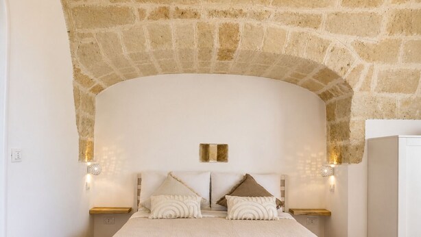 A bedroom with a stone arch ceiling, a bed with two pillows, two bedside tables, and a white wardrobe. - Tenuta Polignano - La Scuderia, a Rural Estate in Puglia.  Exposed Stone Arches (Puglia)