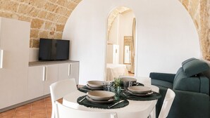 A dining area with a stone wall, a television, and a sofa. - Tenuta Polignano - La Scuderia, a Rural Estate in Puglia.  Exposed Stone Arches (Puglia)