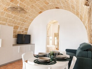 A dining area with a stone wall, a television, and a sofa. - Tenuta Polignano - La Scuderia, a Rural Estate in Puglia.  Exposed Stone Arches (Puglia)