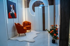 A modern interior with a white shag rug, two orange armchairs, a potted plant with orange flowers, and a framed artwork on the wall. - Cozy Keys Luxury Apartments (Abuja)