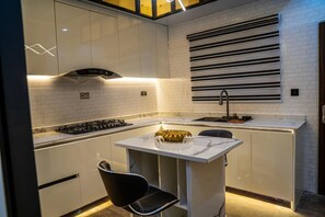 A compact kitchen with a gas stove, a sink, and a small dining area with a chair and a decorative bowl. - Cozy Keys Luxury Apartments (Abuja)