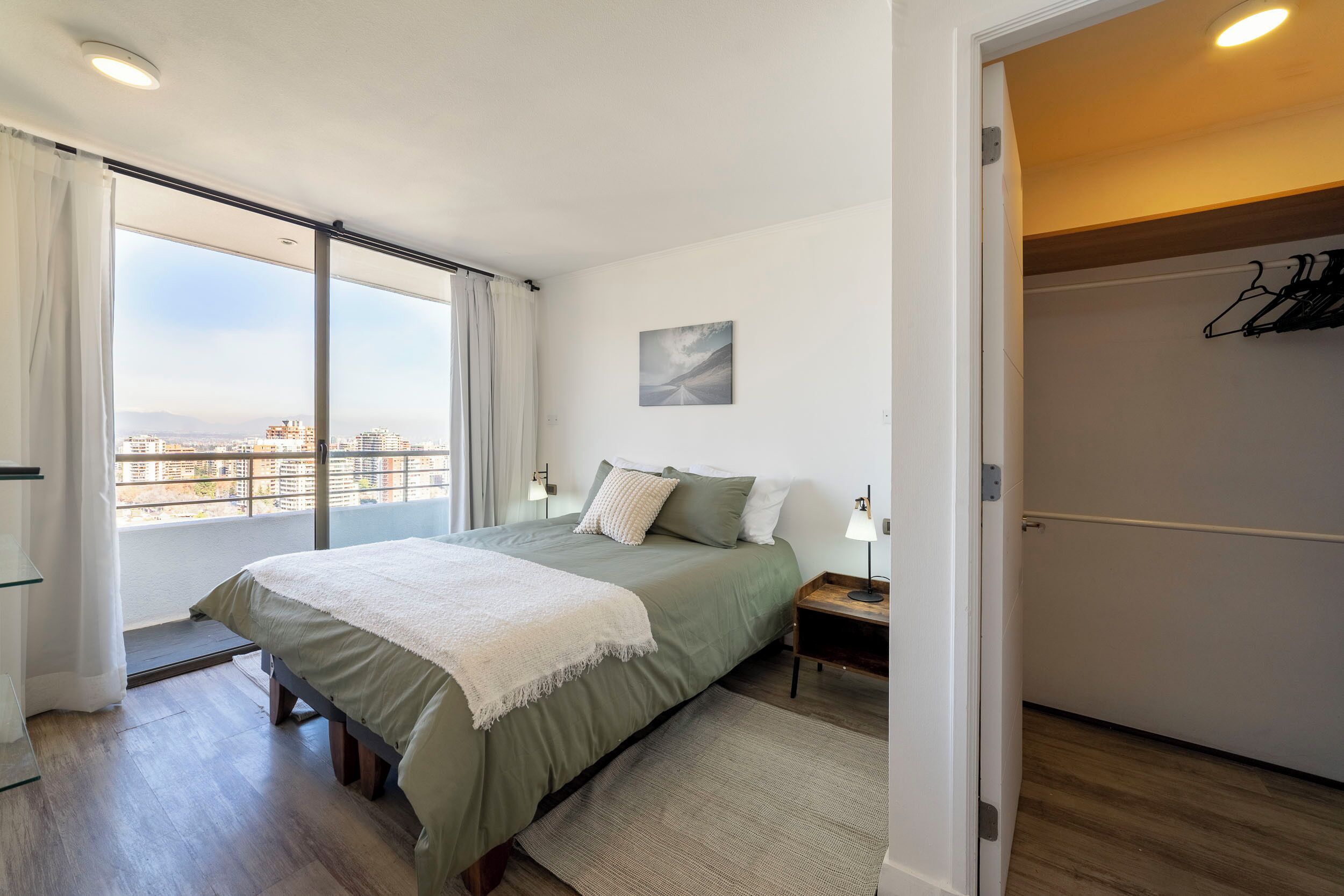 A bedroom with a bed, bedside tables, a view through a sliding door, and a painting on the wall.