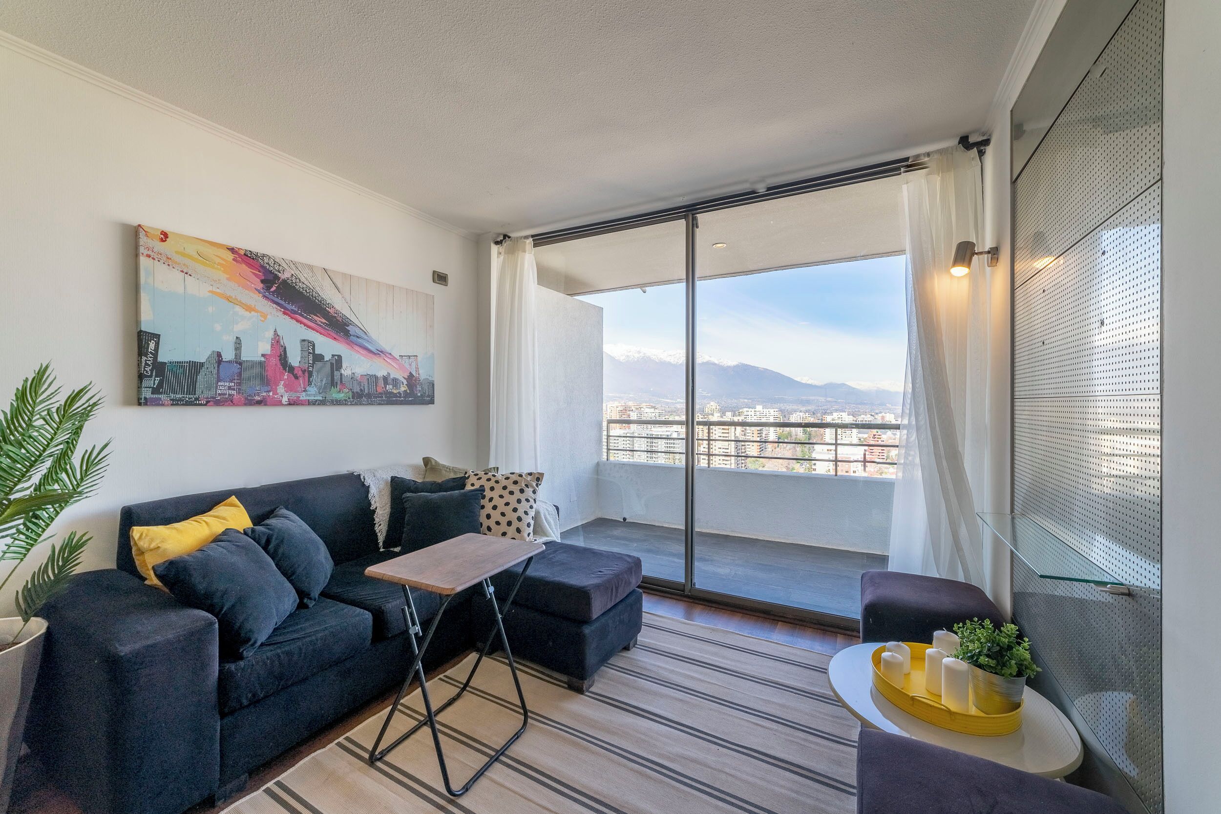 Een moderne woonkamer met een bank, een klein tafeltje en een uitzicht op een stadsgezicht door grote ramen.